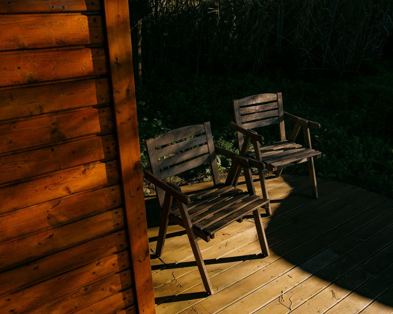 Wooden chairs on a sunlit wood deck beside a cabin wall